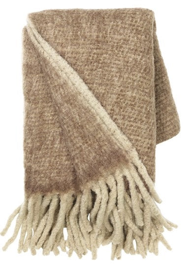 Pläden Mathea från Cozy Living i brun har en tjock och mjuk känsla. Perfekt för kyliga kvällar och är detaljen som sätter den perfekta touchen i soffan eller på sängen. Den mysiga pläden är i en ljusbrun melerad ullblandning med alpacka.